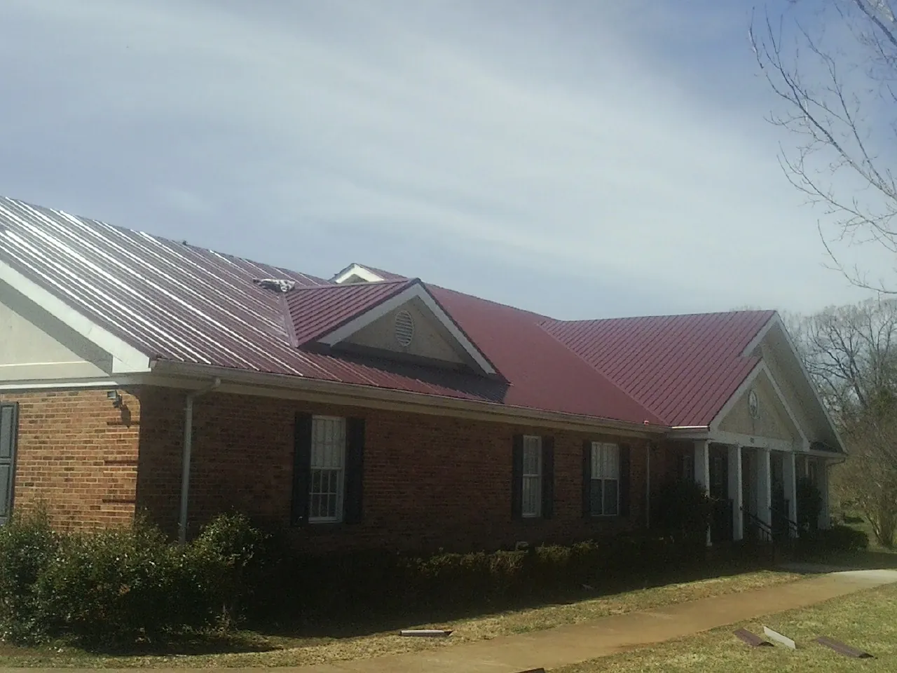 Red metal roof with gabled entries on a long brick building, from a Hail Damage Roof Repair job in Riva