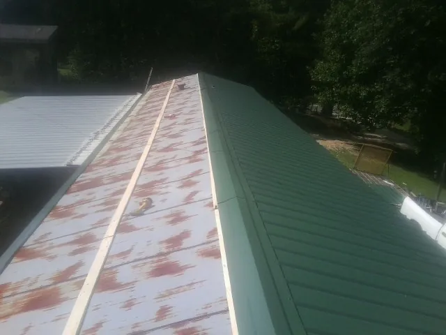Old rusted panels beside newly installed green metal roofing — Wind Damage Roof Repair by Roofing Brothers in Riva
