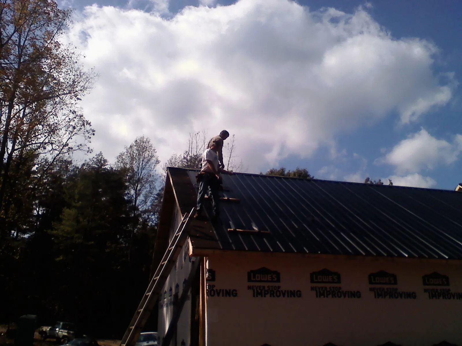Roofer fastening dark metal panels high against a cloudy sky, from a Roof Inspection job in Riva