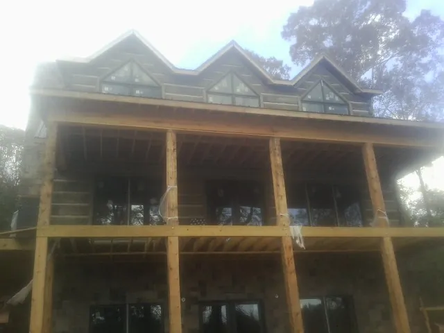 Dormers and porch framing on a large log home under construction — Roof Coating work by our crew in Riva