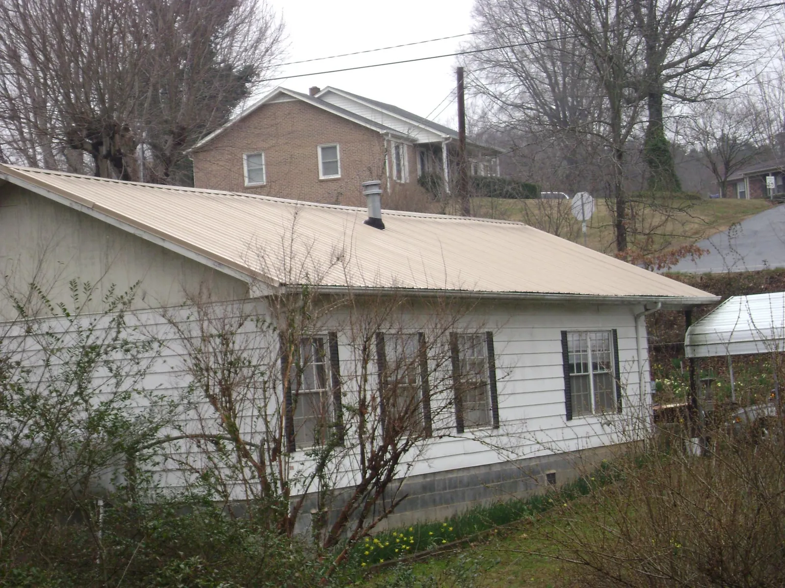 Tan metal roof on a white sided house set into a hillside — Commercial Roofing by Roofing Brothers in Riva