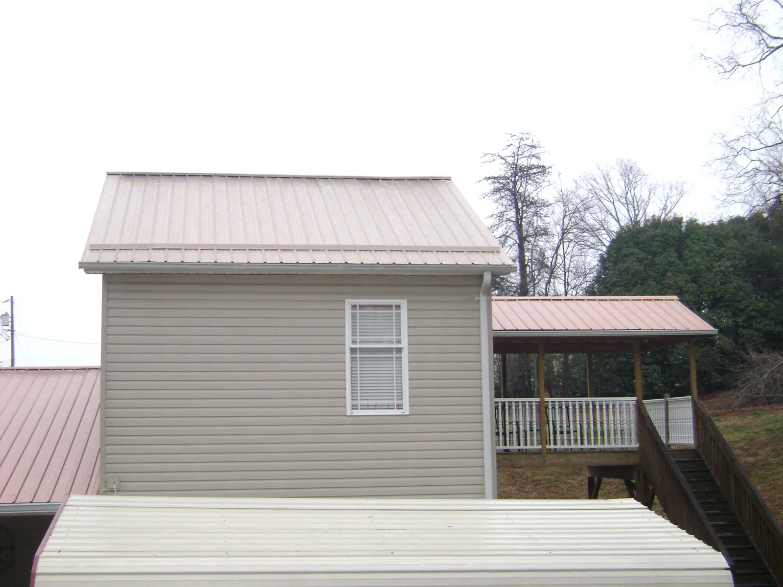 Tan metal roofs on a two story addition and attached porch, from a Roof Replacement job in Riva